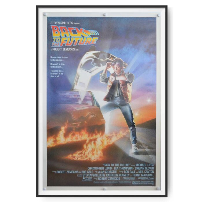 This is an original US cinema Poster for the Film 'Back to the Future'. The poster shows Marty McFly (played by Michael J Fox) standing beside the time travelling DeLorean car.